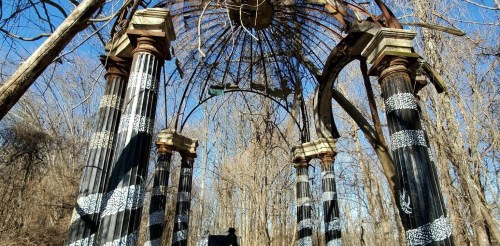 A weathered structure with tall columns and a broken roof, surrounded by bare trees against a clear blue sky.