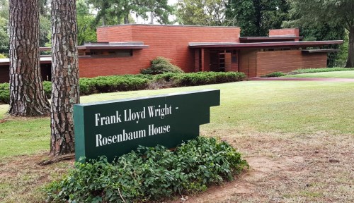 Sign for the Frank Lloyd Wright Rosenbaum House, with the house visible in the background surrounded by greenery.
