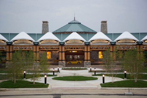A modern building with a peaked roof, stone accents, and landscaped pathways, illuminated at dusk.