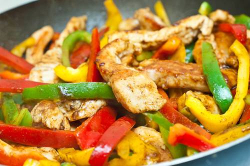 Sautéed chicken strips with colorful bell peppers in a skillet, showcasing vibrant red, yellow, and green vegetables.