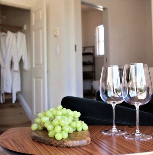 A cozy room featuring two wine glasses and a cluster of green grapes on a wooden table, with bathrobes in the background.