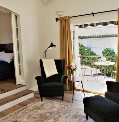 Cozy living space with green armchairs, a small table, and a view of a balcony with plants and a table set outside.