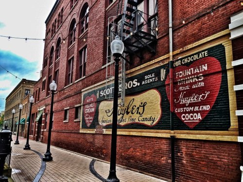 Historic brick wall featuring vintage advertisements for ice cream and chocolate, with street lamps and a cobblestone path.