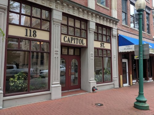 Facade of a building on Capitol Street, featuring large windows and a door, with a nearby blue awning.