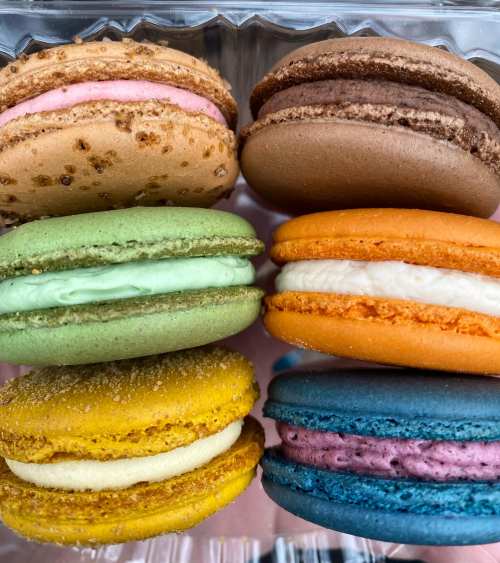 A colorful assortment of six macarons in various flavors, including pink, brown, green, orange, yellow, and blue.