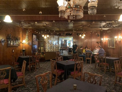 A cozy restaurant interior with wooden walls, chandeliers, and tables set for dining, featuring a small group of diners.