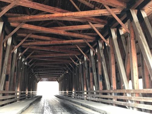 Interior view of a wooden covered bridge, showcasing its intricate beams and a bright light at the far end.