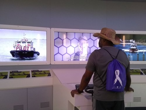 A person in a straw hat watches an interactive display about boats and navigation at an exhibit.