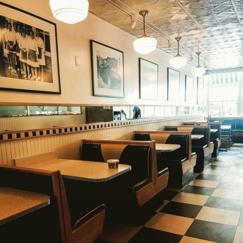 A retro diner interior with empty booths, black and white checkered floor, and vintage photographs on the walls.