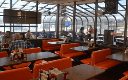 A bright diner interior with orange booths, tables, and condiments, featuring patrons enjoying their meals.
