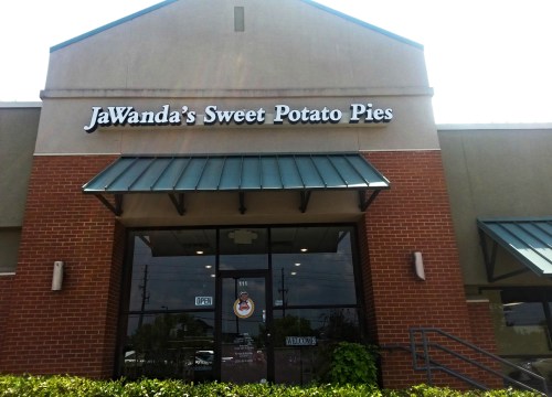 Sign for "JaWanda's Sweet Potato Pies" on a storefront with an open sign and green awning.