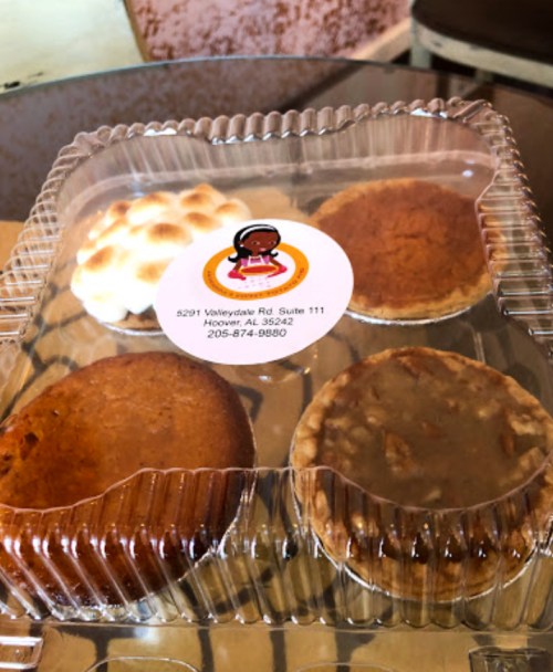 A clear container holding four assorted desserts, including pies and a topped treat, with a label on the lid.
