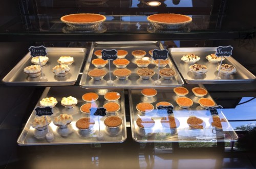 A display case filled with various desserts, including pies and cupcakes, labeled with flavors like pecan and s'mores.