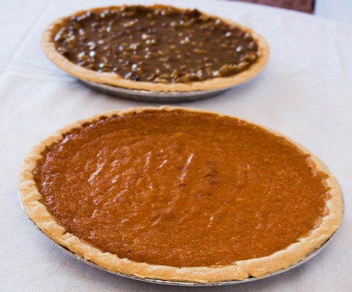 Two pies on a table: one pumpkin pie with a smooth orange filling and one chocolate pie with a glossy brown filling.