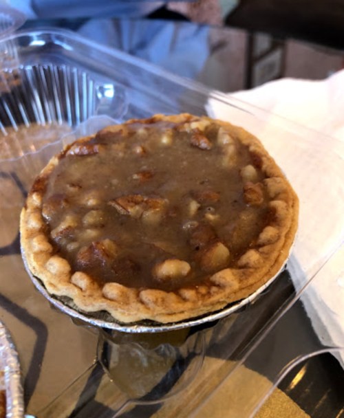 A small pie with a golden crust filled with a brown, chunky filling, placed in a clear plastic container.