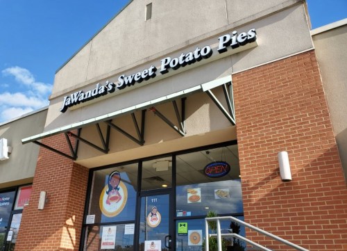 Exterior of JaWanda's Sweet Potato Pies shop, featuring a sign and an open door under a blue sky.