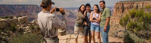 A group of four people poses for a photo at the Grand Canyon, with one person taking the picture.