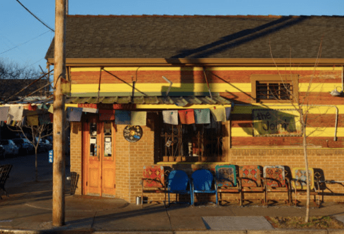 Colorful restaurant exterior with a yellow and brick facade, featuring outdoor seating and decorative laundry hanging above.