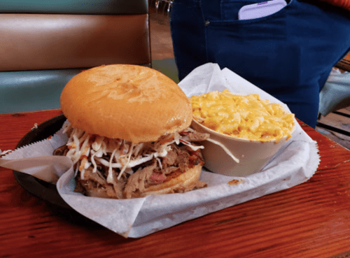 A pulled pork sandwich with coleslaw on a bun, served with a side of creamy macaroni and cheese.