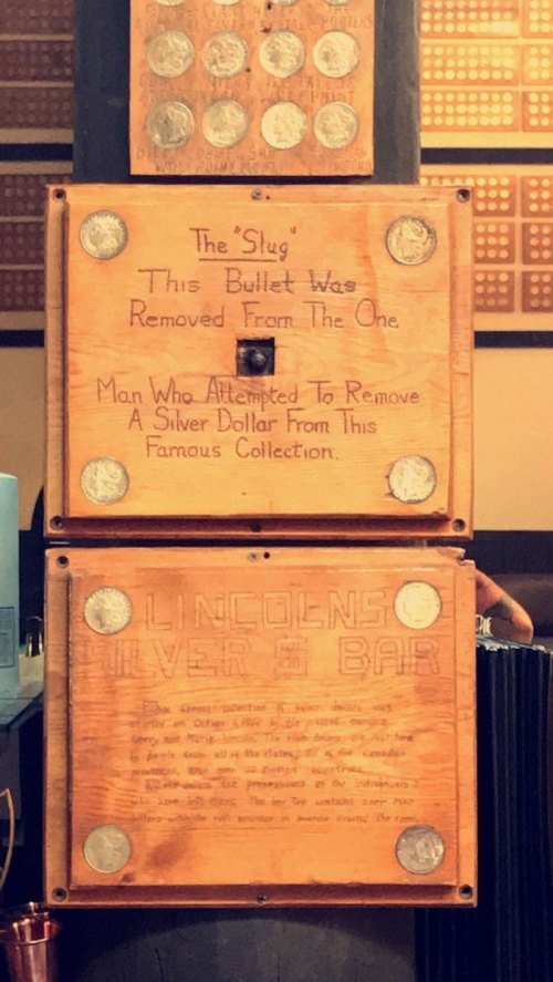 Wooden plaques display text about a bullet and a man who tried to remove a silver dollar from a famous collection.