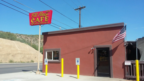 Exterior of El Rey Café with a red building, American flag, and a bright sign against a clear blue sky.