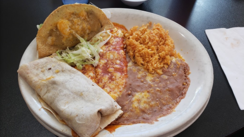 A plate of Mexican food featuring a taco, burrito, rice, and refried beans, garnished with lettuce.