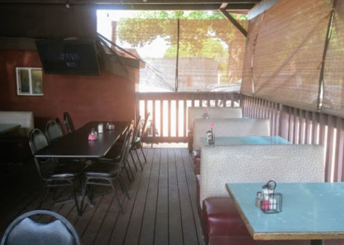 Outdoor dining area with tables and chairs, featuring a TV and shaded by bamboo blinds.