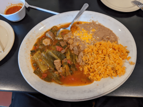 A plate of food featuring meat with vegetables, refried beans, and orange rice, served with a spoon.