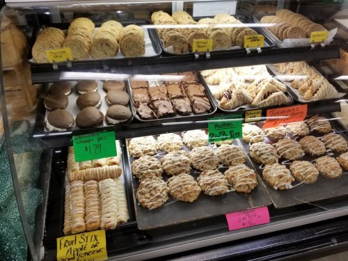 A display case filled with various baked goods, including cookies, muffins, and pastries, with price tags visible.