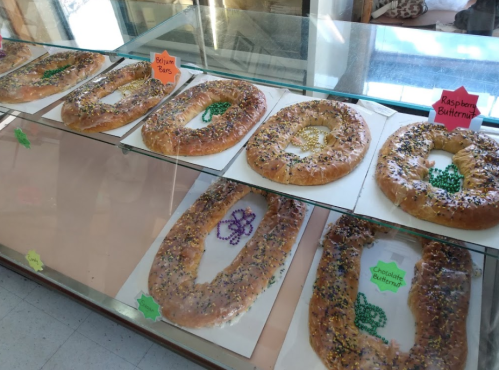 A display case filled with colorful king cakes, each decorated with sprinkles and labeled with different flavors.
