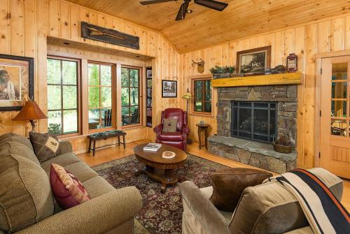 Cozy wooden living room with a stone fireplace, comfortable seating, and large windows letting in natural light.