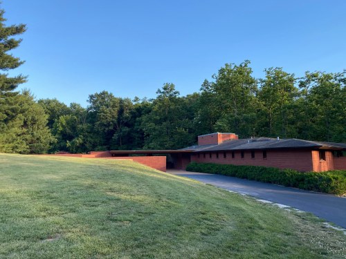 A modern brick building set against a backdrop of trees and a clear blue sky, with a grassy area in the foreground.