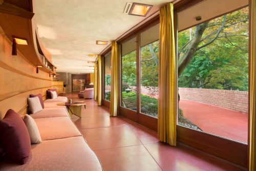 A cozy interior with a long bench, large windows, and a view of lush greenery outside. Warm lighting enhances the space.