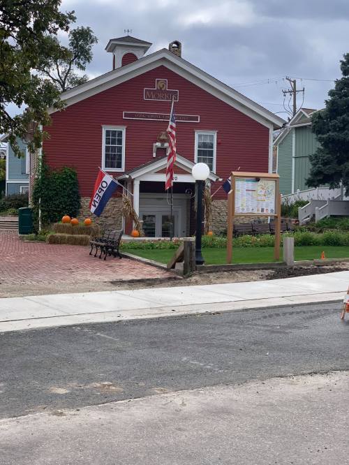 A red building with flags and pumpkins in front, featuring a sign that says "Open" and a map display nearby.
