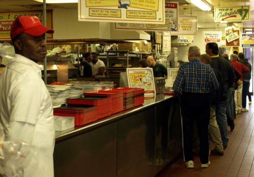 A busy diner with a long line of customers waiting to order, featuring a man in a red cap at the counter.