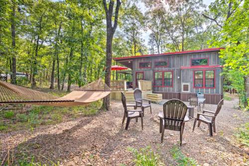 A cozy cabin in a wooded area, featuring a hammock, outdoor seating, and a red umbrella on the porch.