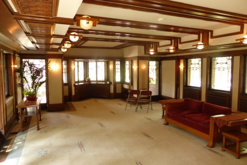 Interior of a spacious room with wooden accents, large windows, a red couch, and two chairs, featuring a light carpet.