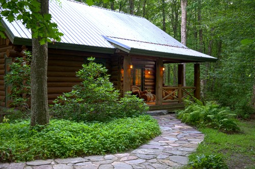A cozy log cabin surrounded by lush greenery and a stone pathway leading to the porch.