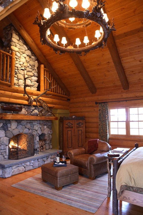 Cozy log cabin interior with a stone fireplace, leather armchair, and rustic chandelier, creating a warm atmosphere.