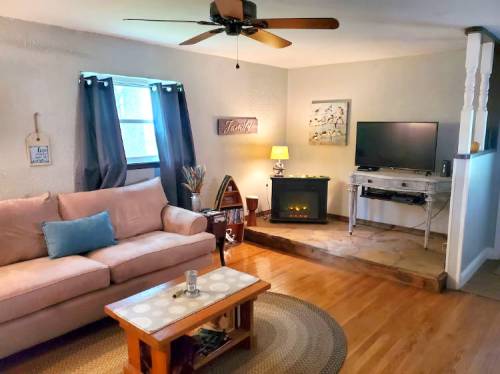 Cozy living room with a pink sofa, coffee table, TV, and a faux fireplace, featuring warm lighting and wooden floors.