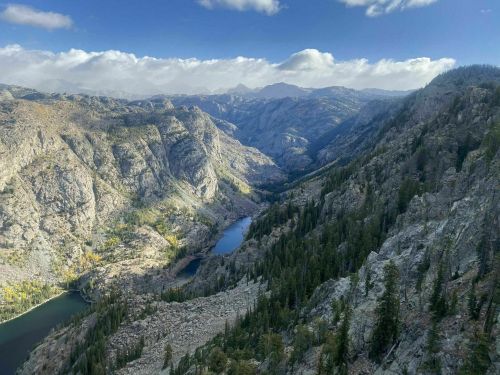 A panoramic view of rugged mountains and valleys, with two blue lakes nestled among the trees and rocky terrain.