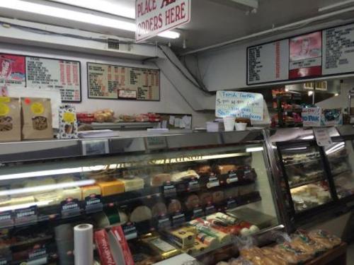 A busy deli counter displaying various baked goods and a menu board with food options above.