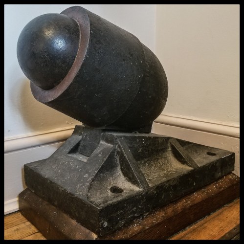 A vintage cannonball resting on a wooden base, positioned at an angle against a wall.
