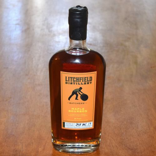 A bottle of Litchfield Distillery Maple Bourbon on a wooden surface, featuring a distinctive label and dark amber liquid.