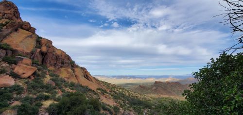 A scenic view of rocky hills and distant mountains under a partly cloudy sky. Lush greenery in the foreground.