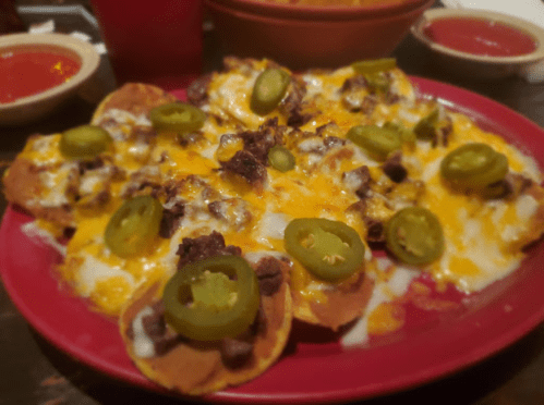 A plate of nachos topped with melted cheese, jalapeños, and beef, served with salsa on the side.