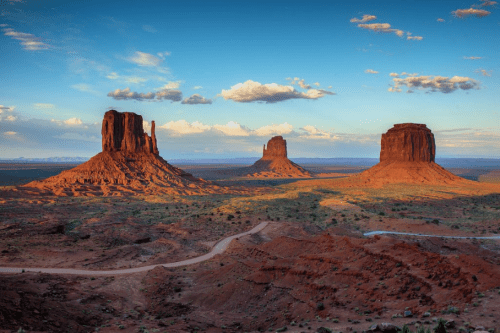 A scenic view of Monument Valley featuring red rock formations under a blue sky with scattered clouds.