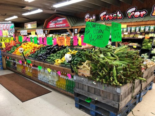 A vibrant farm market display featuring colorful fruits and vegetables, with signs indicating prices and fresh produce.