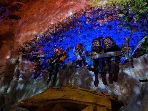 Colorful gnome figures playing instruments on a rocky surface, illuminated by blue and purple lights.