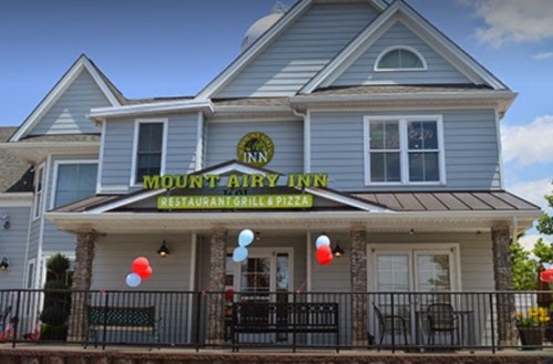 Exterior of Mount Airy Inn with a sign, featuring a porch decorated with red, white, and blue balloons.